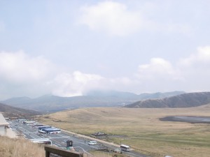 草千里展望所から見下ろす阿蘇火山博物館の駐車場と草千里の高原の画像